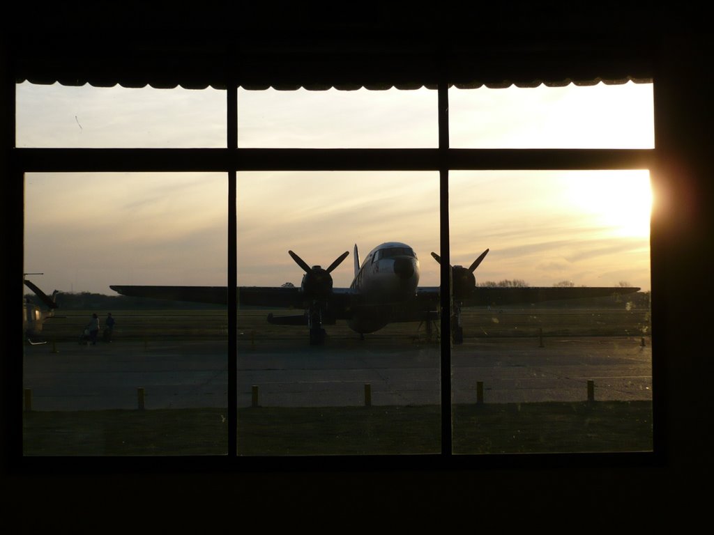 Desde el pasillo del museo, un viejo avión mientras el sol cae by Ruben Pouquette