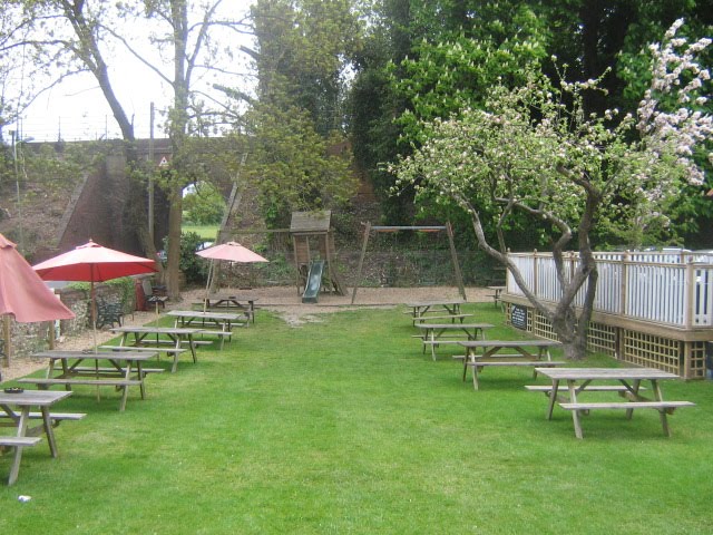 The French Horn narrow garden, filled with wooden picnic tables and a little wooden play equipment by Robert'sGoogleEarthPictures