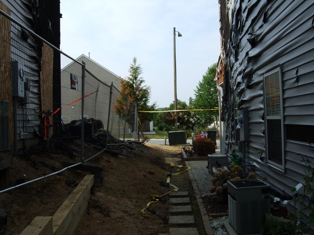 The corridor between two closely spaced suburban houses, the one on the left had just had a huge fire, which melted the vinyl siding on the one on the right, and even killed some of the branches on the tree across the street, 6-26-09 by tompope2001