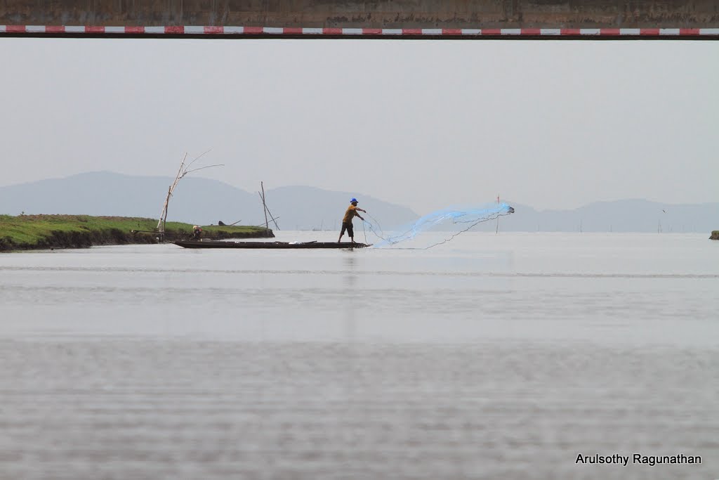 Fisherman casts his net into channel leading to Thale Luang, with Elevated Road in the foreground. Thale Noi Waterfowl Reserve, Khuan Khanun District, Phatthalung Province, Southern Thailand. by Arul KL