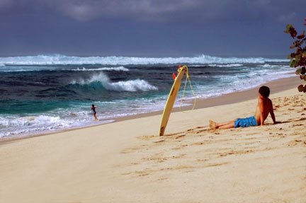 Surfer sitting on sand, Sunset Beach by photosofaloha