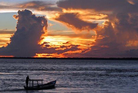 Ein Fischer verlässt bei Sonnenuntergang seinen kleinen Ort am Amazonas und geht an seine Arbeit. Coari, Brasilien by dia.ch